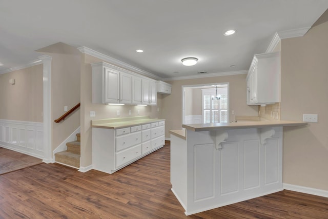 kitchen featuring a breakfast bar, dark wood-type flooring, kitchen peninsula, ornamental molding, and white cabinetry