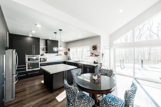 kitchen with decorative light fixtures, a kitchen island, decorative backsplash, sink, and stainless steel appliances