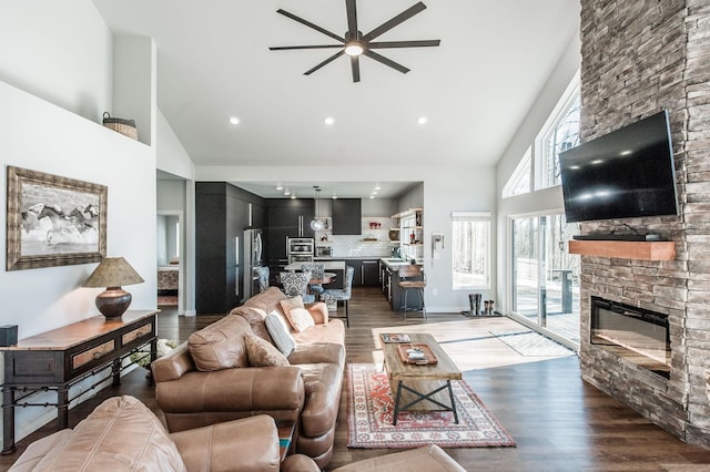 living room featuring ceiling fan, sink, a high ceiling, a stone fireplace, and dark hardwood / wood-style flooring