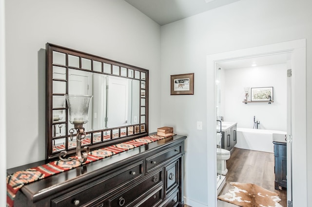 bathroom with hardwood / wood-style floors, toilet, a bath, and vanity