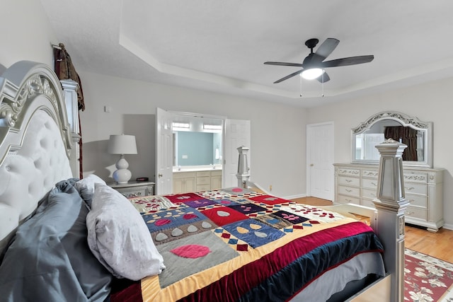 bedroom with ceiling fan, light wood-type flooring, connected bathroom, and a tray ceiling