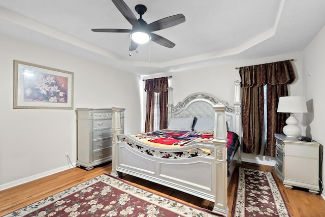 bedroom featuring a raised ceiling, ceiling fan, and light wood-type flooring