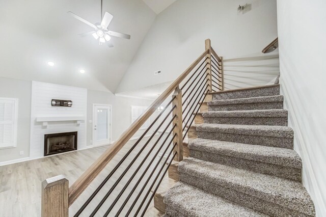 stairway with ceiling fan, wood finished floors, a fireplace, high vaulted ceiling, and recessed lighting