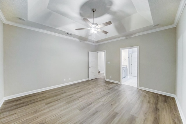 unfurnished bedroom featuring a raised ceiling, visible vents, light wood-style floors, ornamental molding, and baseboards