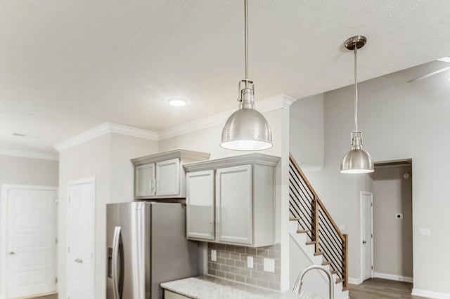 kitchen with pendant lighting, light countertops, crown molding, and stainless steel refrigerator with ice dispenser