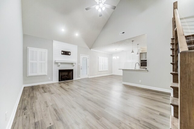 unfurnished living room featuring baseboards, light wood-style flooring, a fireplace, a sink, and ceiling fan with notable chandelier