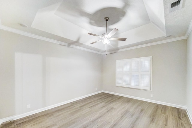 empty room with baseboards, ceiling fan, wood finished floors, a tray ceiling, and crown molding