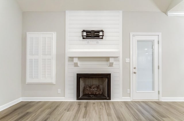 unfurnished living room with a fireplace, baseboards, vaulted ceiling, and wood finished floors