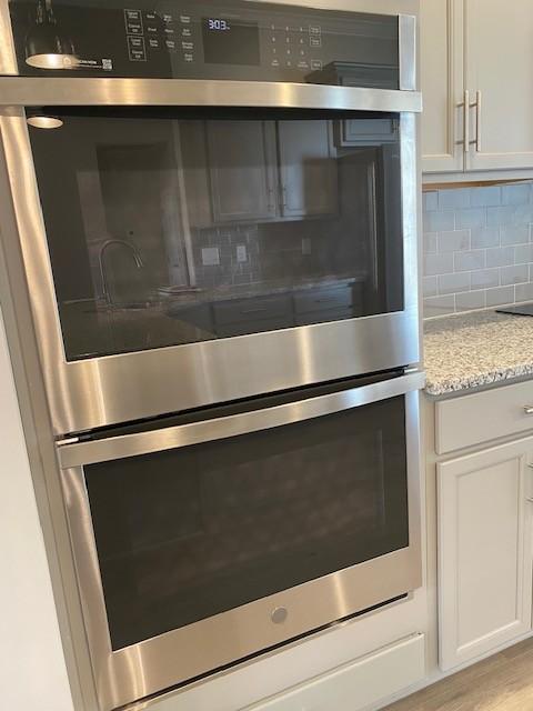 room details with double oven, white cabinetry, tasteful backsplash, and light wood-style flooring