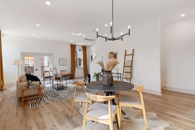 dining area with french doors, light wood-type flooring, and an inviting chandelier