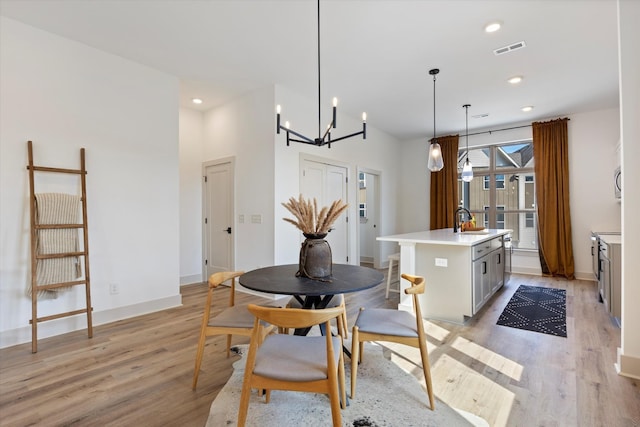 kitchen with decorative light fixtures, a kitchen island with sink, light hardwood / wood-style floors, and a notable chandelier