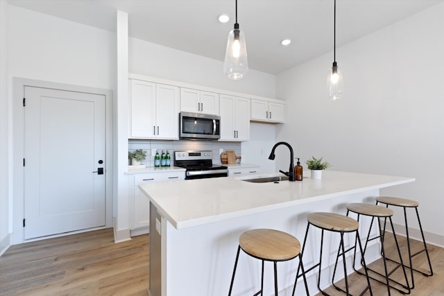 kitchen with pendant lighting, sink, stainless steel appliances, and a kitchen island with sink