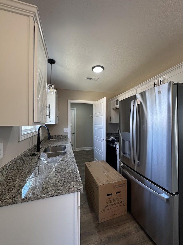 kitchen with visible vents, dark wood-type flooring, white cabinets, a sink, and stainless steel fridge