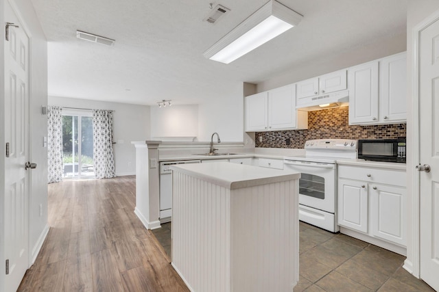 kitchen featuring kitchen peninsula, white appliances, dark wood-type flooring, sink, and a center island