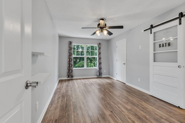 empty room featuring wood-type flooring, a barn door, and ceiling fan