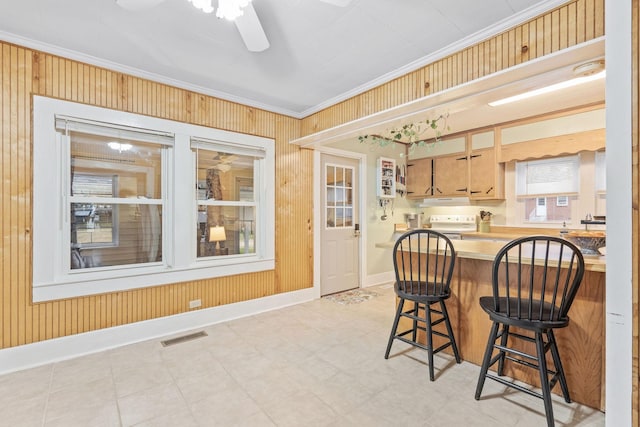 kitchen featuring ceiling fan, wood walls, a breakfast bar area, light brown cabinetry, and ornamental molding