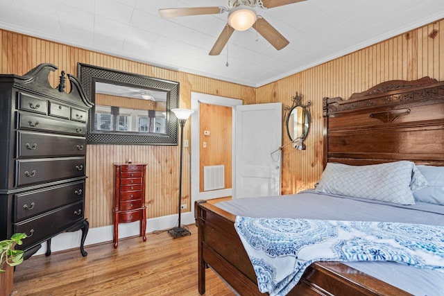 bedroom with hardwood / wood-style flooring, ceiling fan, crown molding, and wood walls