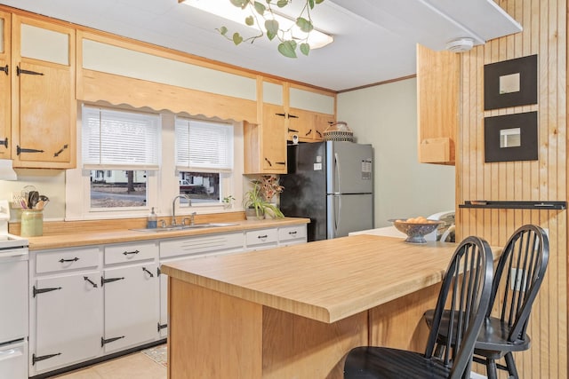 kitchen with wood counters, stainless steel fridge, a kitchen breakfast bar, sink, and white stove