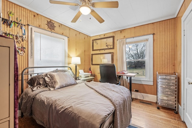 bedroom with ceiling fan, light hardwood / wood-style flooring, crown molding, and wooden walls