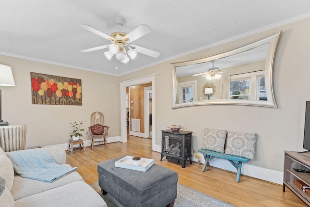 living room featuring hardwood / wood-style flooring, a wood stove, ceiling fan, and ornamental molding