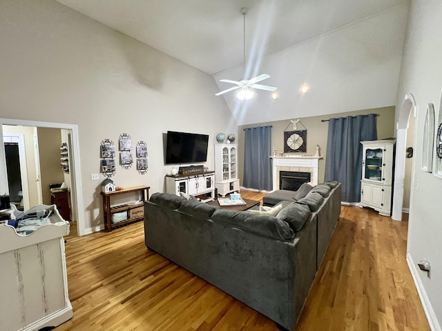 living room with a fireplace, light wood-type flooring, high vaulted ceiling, and ceiling fan