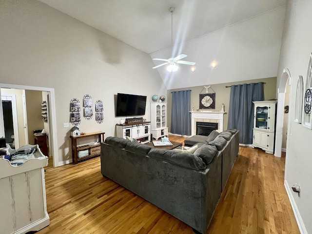 living room with a tile fireplace, ceiling fan, high vaulted ceiling, and light hardwood / wood-style floors