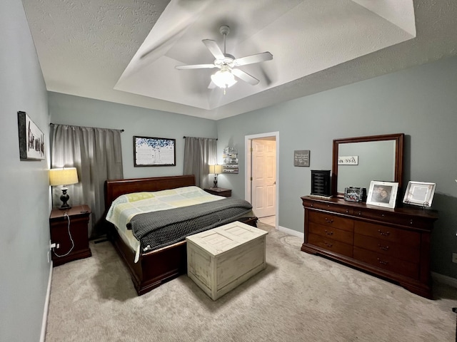 carpeted bedroom featuring a tray ceiling, ceiling fan, and a textured ceiling