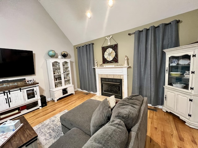 living room with a tile fireplace, light hardwood / wood-style flooring, and lofted ceiling