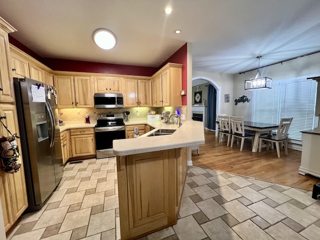 kitchen with kitchen peninsula, light brown cabinetry, backsplash, stainless steel appliances, and sink