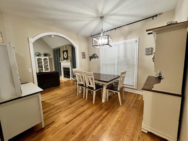 dining space featuring a tile fireplace, light hardwood / wood-style floors, lofted ceiling, and a notable chandelier