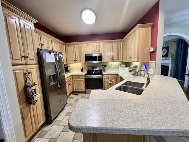 kitchen featuring kitchen peninsula, appliances with stainless steel finishes, decorative backsplash, light brown cabinetry, and sink