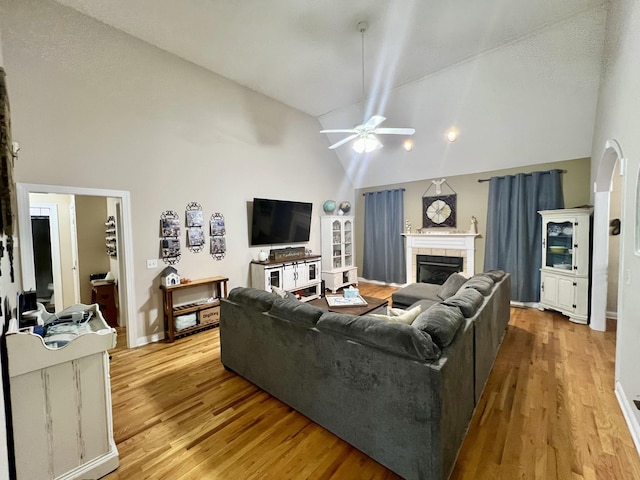 living room featuring a fireplace, light wood-type flooring, high vaulted ceiling, and ceiling fan