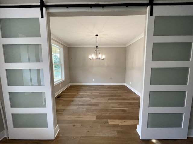 unfurnished dining area with a barn door, hardwood / wood-style flooring, crown molding, and a notable chandelier