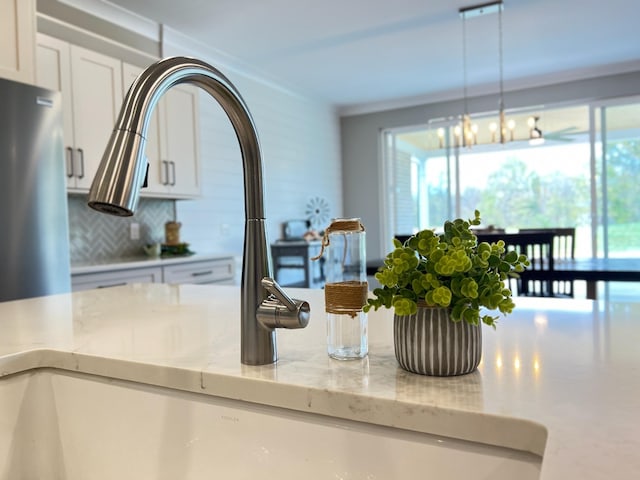 details with backsplash, light stone counters, pendant lighting, a notable chandelier, and white cabinetry