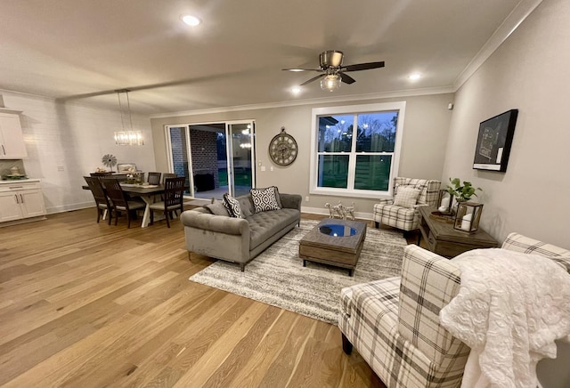 living room with ceiling fan with notable chandelier, light hardwood / wood-style floors, and crown molding