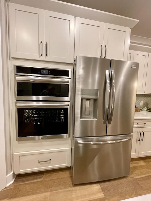 kitchen with white cabinetry, light hardwood / wood-style flooring, appliances with stainless steel finishes, and tasteful backsplash