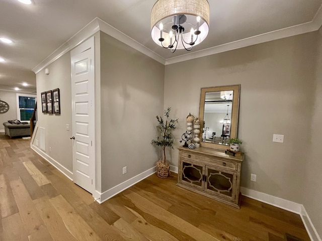 hallway with hardwood / wood-style floors, crown molding, and an inviting chandelier