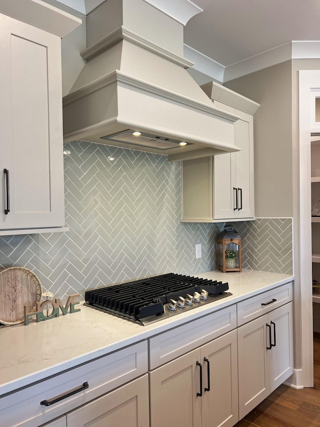 kitchen with premium range hood, dark hardwood / wood-style floors, light stone countertops, tasteful backsplash, and gas cooktop