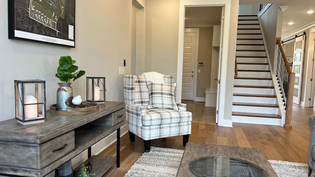 living area featuring a barn door, wood-type flooring, and ornamental molding