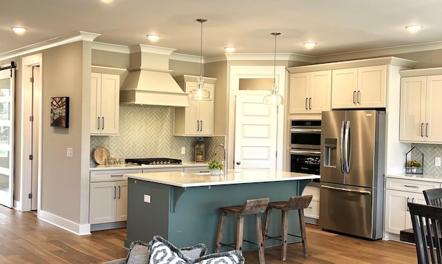 kitchen with appliances with stainless steel finishes, a kitchen island with sink, a barn door, decorative light fixtures, and white cabinetry