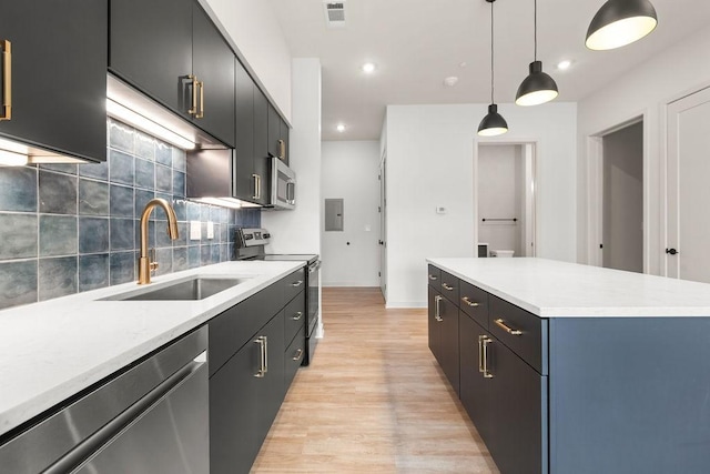 kitchen with sink, stainless steel appliances, decorative light fixtures, decorative backsplash, and light wood-type flooring