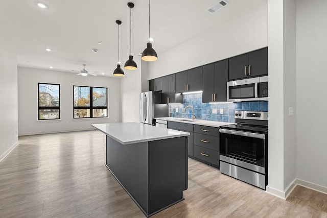 kitchen with ceiling fan, light hardwood / wood-style floors, pendant lighting, a kitchen island, and appliances with stainless steel finishes