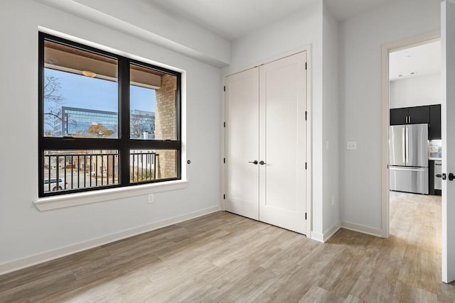 unfurnished bedroom with light hardwood / wood-style floors, stainless steel refrigerator, and a closet