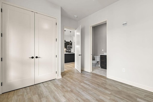 unfurnished bedroom featuring ensuite bath, a closet, and light hardwood / wood-style flooring