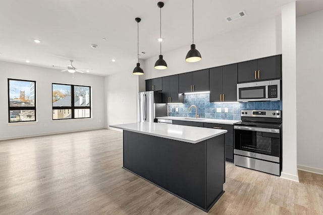 kitchen with ceiling fan, a kitchen island, decorative light fixtures, and appliances with stainless steel finishes