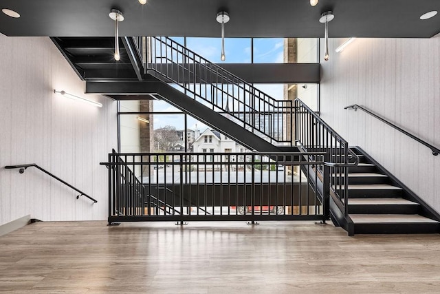 staircase featuring wooden walls, a towering ceiling, and hardwood / wood-style flooring