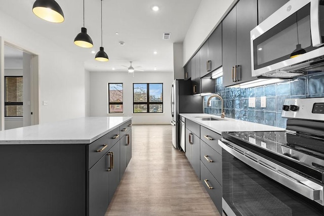 kitchen featuring appliances with stainless steel finishes, ceiling fan, sink, decorative light fixtures, and a kitchen island