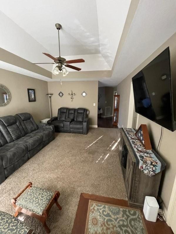 carpeted living room featuring a raised ceiling and ceiling fan