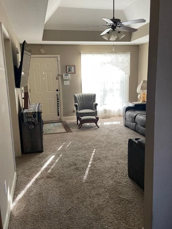 carpeted living room with a tray ceiling and ceiling fan