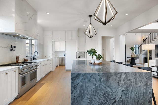 kitchen featuring white cabinetry, a spacious island, decorative light fixtures, range with two ovens, and exhaust hood